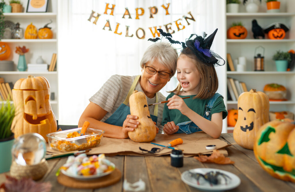 Grandmother and granddaughter painting pumpkins on Halloween